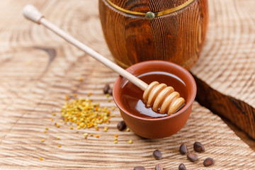 Flower pollen on a wooden textured background and a spoon with fragrant honey in a glossy bowl.