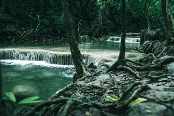 view of a beautiful waterfall in Thailand in a green jungle and clean environment in a moody green tone look surrounded with big trees and clear fresh green water which suggests an eco environment
