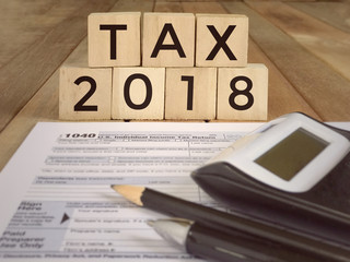 United States federal income tax return IRS 1040 documents, with pen, pencil, calculator and wooden blocks with ‘TAX 2018’ written on them.