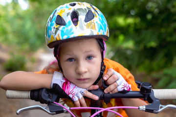 Cute little sad girl in a helmet with a bike in the summer