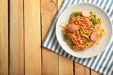 Plate with delicious pasta and sausage on wooden table
