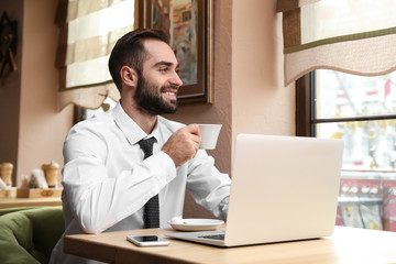 Young businessman drinking coffee while working on laptop in cafe