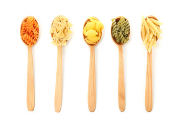 Spoons with assortment of uncooked pasta on white background
