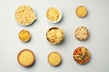 Bowls with assortment of uncooked pasta on grey background