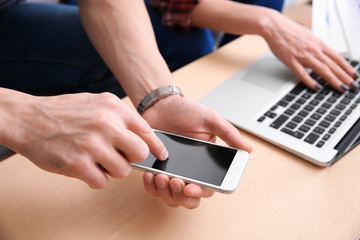 Young man working with mobile phone in modern office, closeup