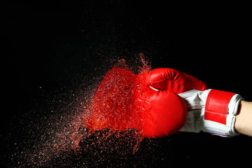 Hand in boxing glove with splashes of liquid on dark background