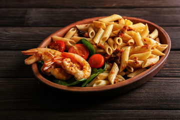Plate of tasty pasta with shrimps and tomatoes on wooden background