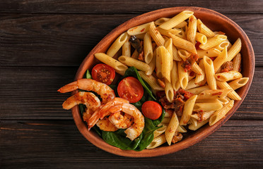 Plate of tasty pasta with shrimps and tomatoes on wooden background