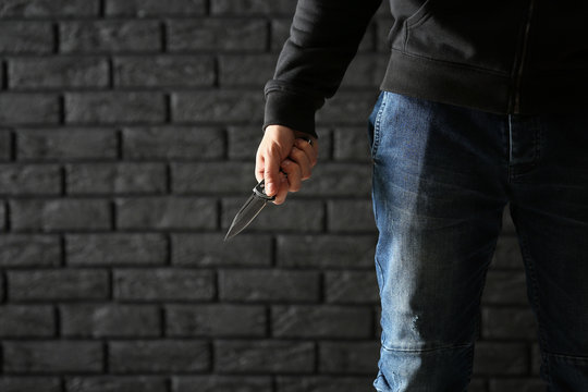 Male criminal with a knife on dark brick background