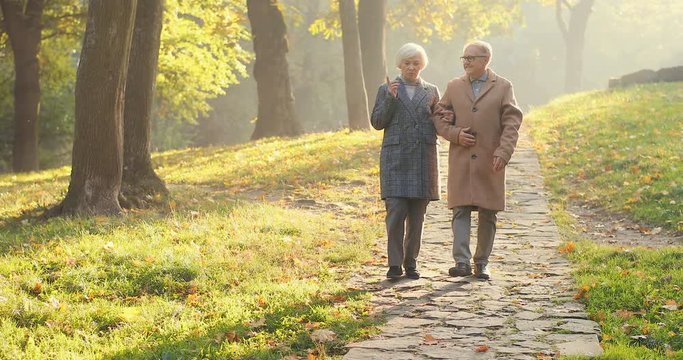 Beautiful romantic picture of an old Caucasian woman and man stepping the park path and holding each other in the autumn. Outside.
