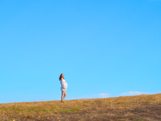 Beautiful pregnant woman in a white woolen sweater. Happy pregnant woman posing on a mown wheat field.