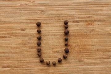 Capital characters made of peppercorns. Alphabet letters on wood background.