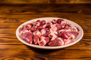 Ceramic plate with raw chicken hearts on wooden table