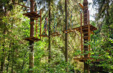 Teen boy on a ropes course in a treetop adventure park passing hanging rope obstacle