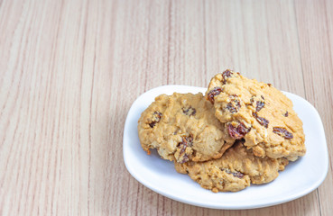 Hearty raisin cookies put on a white plate. The background is tiled flooring mimics wood.