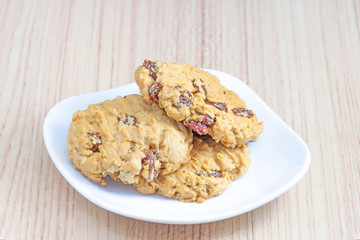 Hearty raisin cookies put on a white plate. The background is tiled flooring mimics wood.