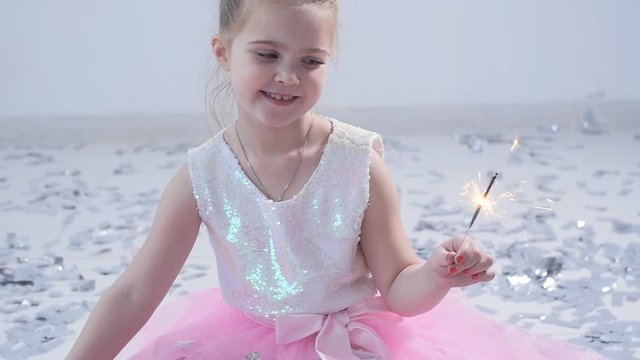 The concept of party and holiday. Happy little girl in a sparkler dress in white interior
