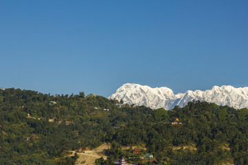 Naklejka premium Annapurna's huge snowy mountain against the backdrop of the village on the green hills under a clear blue sky.