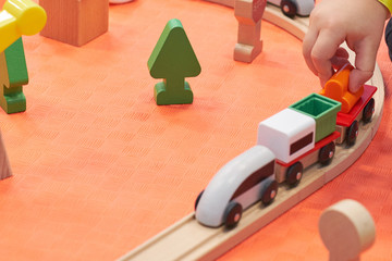 Children playing with wooden train. Toy railroad. Toddler kid and baby play with blocks, trains and cars. Educational toys for preschool and kindergarten child. View from above, kids on the floor.