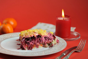 Herring under a Fur Coat. Traditional Russian cuisine salad. Next to the plate are cutlery, tangerines, a candle. Red background. Close-up.