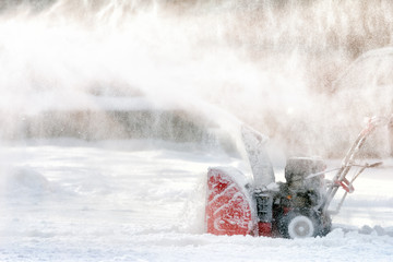 worker cleaning white snow by using snow blower on sunny winter wonderland day against sun...