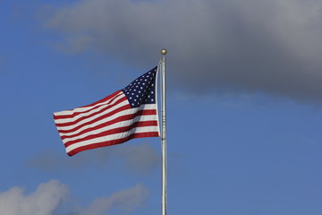 US Flag flying in the wind with blue sky and white clouds.