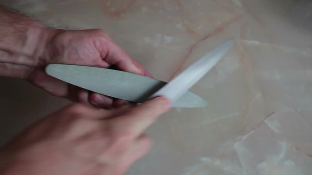 The chef sharpens the big kitchen knife. The man holds the grindstone and sharpens the knife.