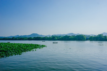 Calm water of West Lake and surrounding hills, with boats traveling on water, in Hangzhou, China
