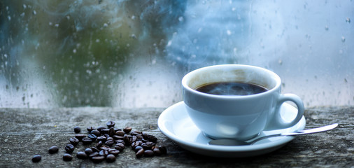 Enjoying coffee on rainy day. Coffee morning ritual. Fresh brewed coffee white mug and beans on windowsill. Wet glass window and cup of hot coffee. Autumn cloudy weather better with caffeine drink