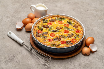 Baked homemade quiche pie in ceramic baking form, eggs and cream