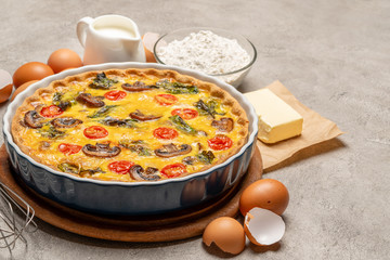 Baked homemade quiche pie in ceramic baking form, eggs and cream