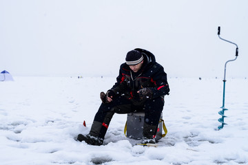 Fototapeta na wymiar Fishing adventures. Fisherman waiting to catch a fish on the lake in winter
