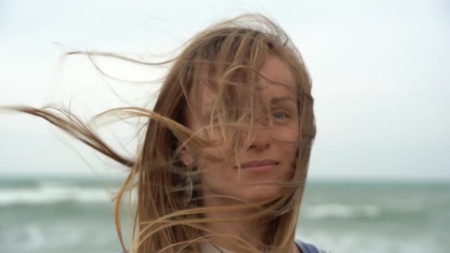 Young woman on the background of the sea waving her head to the side and fluttering hair in the wind. Charming  blonde girl on sea coast. Beautiful woman enjoys a wind, the feeling of freedom