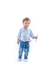 A portrait of a small dark-skinned boy with curly hair in jeans and a light-colored shirt is standing in a half-turn holding pencils in both hands and looking to the side