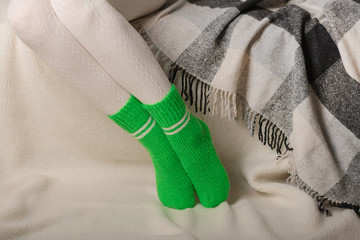 Female legs in warm white knitted tights and green socks on a white background made of faux fur