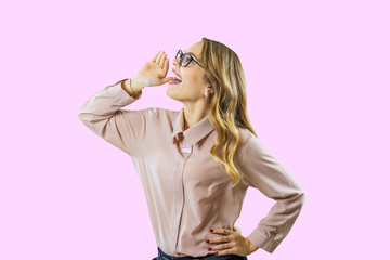 Excited blonde girl in shirt and glasses stands sideways and screams on an isolated blue background