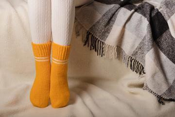 Female legs in warm white knitted tights and yellow socks on a white background made of faux fur