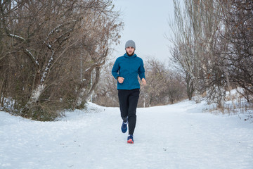 Young male runner training outdoors in winter times, man run on the snow 