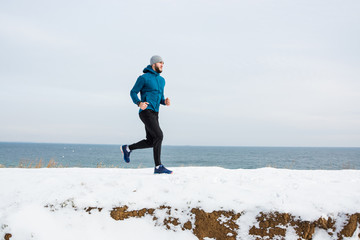 Young male runner training outdoors in winter times, man run on the snow 