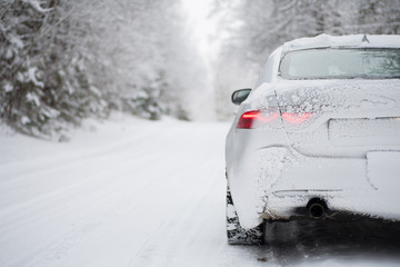 Closeup of a white saloon (sedan) car driving along a snowy forest road covered in heavy snow