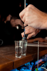 Fototapeta na wymiar Bartender pours alcoholic drink into small glasses on bar