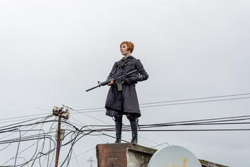Young woman in modern black techwear style with rifle posing on the rooftop, portrait of redhead woman cyperpunk or   post apocalyptic concept