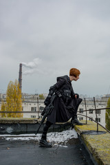 Young woman in modern black techwear style with rifle posing on the rooftop, portrait of redhead woman cyperpunk or   post apocalyptic concept