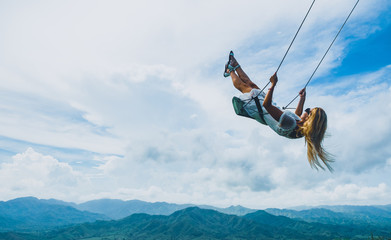 Blond girl swinging in the air over the mountains in summer