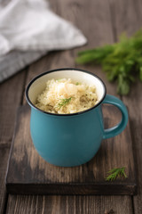 Porridge with butter, fresh herbs in a cup on a dark wooden board