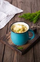 Porridge couscous with butter, fresh herbs in a cup on a dark wooden board