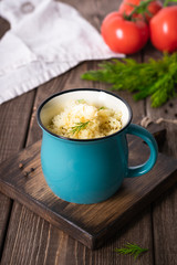 Couscous with butter, fresh herbs and tomatoes in a turquoise cup on a wooden table