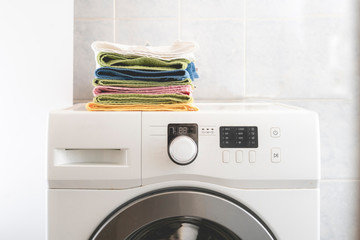 pile of colorful towels lay in the laundry on washing machine and table b