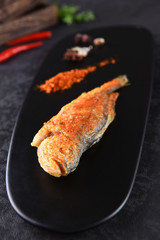 A fried fish with cumin powder in a black dish
