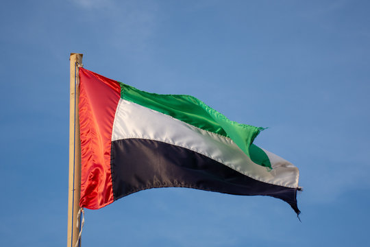United Arab Emirates (UAE) flag blowing in the wind on a sunny blue sky day.